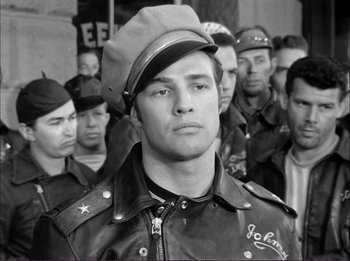 Movie still from “The Wild One” (1953), directed by Laslo Benedek – Black and white photograph of a man in a leather jacket and hat; Close Up shot, Over the shoulder angle