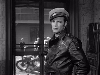 Movie still from “The Wild One” (1953), directed by Laslo Benedek – A black and white photo of a man in a leather jacket and hat; Medium shot, Low angle