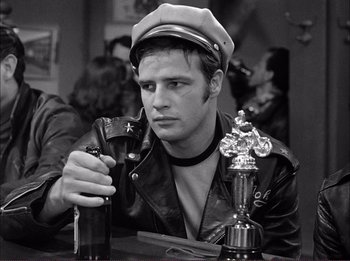 Movie still from “The Wild One” (1953), directed by Laslo Benedek – A man in a leather jacket holding a beer; Medium shot, Over the shoulder angle