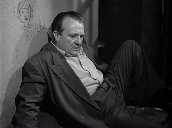 Movie still from “The Wild One” (1953), directed by Laslo Benedek – A black and white photo of a man sitting on a couch; Medium shot, High angle