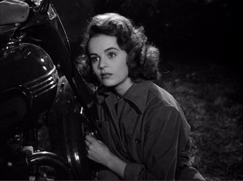 Movie still from “The Wild One” (1953), directed by Laslo Benedek – A woman sitting next to a motorcycle in a black and white photo; Close Up shot, High angle
