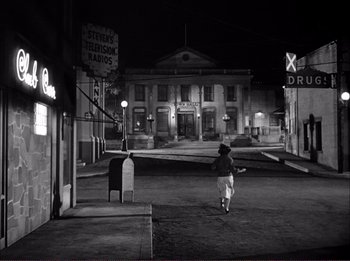 Movie still from “The Wild One” (1953), directed by Laslo Benedek – A person walking down a street at night; Extreme Wide shot, High angle