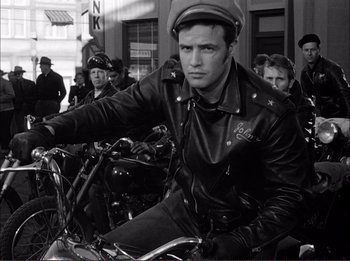 Movie still from “The Wild One” (1953), directed by Laslo Benedek – A black and white photo of a man riding a motorcycle; Medium shot, Low angle