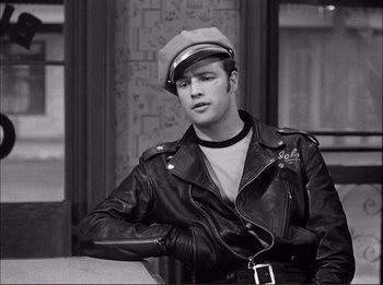 Movie still from “The Wild One” (1953), directed by Laslo Benedek – Black and white photograph of a man in a leather jacket and hat; Medium shot, Over the shoulder angle