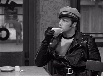 Movie still from “The Wild One” (1953), directed by Laslo Benedek – A man in a leather jacket drinking a cup of coffee; Medium shot, Over the shoulder angle