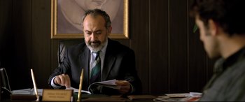 Movie still from “The Wild Pear Tree” (2018), directed by Nuri Bilge Ceylan – A man sitting at a table reading a piece of paper; Medium shot, Low angle