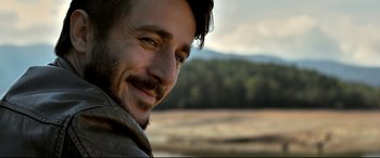 Movie still from “The Wild Pear Tree” (2018), directed by Nuri Bilge Ceylan – A person smiling with trees in the background; Close Up shot, Over the shoulder angle