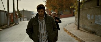 Movie still from “The Wild Pear Tree” (2018), directed by Nuri Bilge Ceylan – A man walking down a street next to another man; Medium shot, Over the shoulder angle