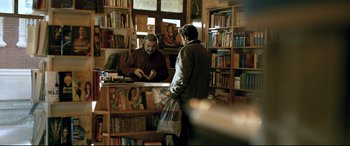 Movie still from “The Wild Pear Tree” (2018), directed by Nuri Bilge Ceylan – A man standing at a book store counter looking at a man holding a bag; Medium shot, Over the shoulder angle