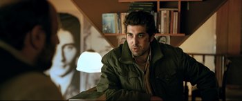 Movie still from “The Wild Pear Tree” (2018), directed by Nuri Bilge Ceylan – A man sitting at a table in front of a book shelf; Medium shot, Over the shoulder angle