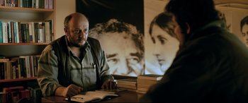Movie still from “The Wild Pear Tree” (2018), directed by Nuri Bilge Ceylan – A man sitting at a table with a stack of books in front of him; Medium shot, Over the shoulder angle