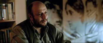 Movie still from “The Wild Pear Tree” (2018), directed by Nuri Bilge Ceylan – A man with a bald head sitting in front of a picture; Close Up shot, Low angle