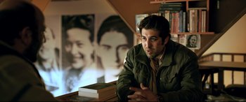 Movie still from “The Wild Pear Tree” (2018), directed by Nuri Bilge Ceylan – A man sitting at a table with a stack of books in front of him; Medium shot, Over the shoulder angle