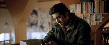 Movie still from “The Wild Pear Tree” (2018), directed by Nuri Bilge Ceylan – A man in a green jacket looking down at a book; Close Up shot, Over the shoulder angle