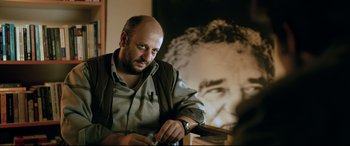Movie still from “The Wild Pear Tree” (2018), directed by Nuri Bilge Ceylan – A man sitting in front of a picture holding a gun; Close Up shot, Low angle