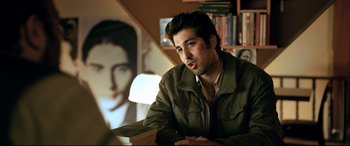 Movie still from “The Wild Pear Tree” (2018), directed by Nuri Bilge Ceylan – A man sitting at a table in front of a picture; Medium shot, Over the shoulder angle
