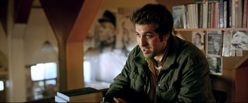 Movie still from “The Wild Pear Tree” (2018), directed by Nuri Bilge Ceylan – A man sitting at a table with a book in front of him; Medium shot, Over the shoulder angle