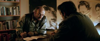 Movie still from “The Wild Pear Tree” (2018), directed by Nuri Bilge Ceylan – A man sitting at a table with another man in front of him; Medium shot, Over the shoulder angle