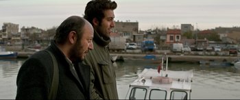 Movie still from “The Wild Pear Tree” (2018), directed by Nuri Bilge Ceylan – A couple of men standing next to each other near a boat; Medium shot, Over the shoulder angle