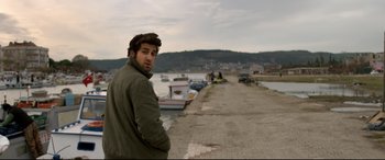 Movie still from “The Wild Pear Tree” (2018), directed by Nuri Bilge Ceylan – A man standing next to a body of water; Medium shot, Over the shoulder angle
