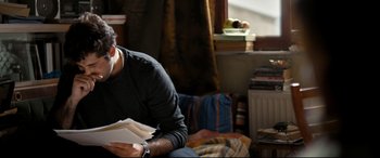 Movie still from “The Wild Pear Tree” (2018), directed by Nuri Bilge Ceylan – A man sitting on a couch looking at papers; Medium shot, Over the shoulder angle