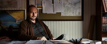 Movie still from “The Wild Pear Tree” (2018), directed by Nuri Bilge Ceylan – A man sitting at a desk in front of a map; Medium shot, Low angle