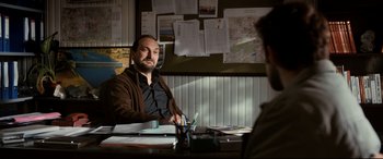 Movie still from “The Wild Pear Tree” (2018), directed by Nuri Bilge Ceylan – A man sitting at a table in front of a map; Medium shot, Over the shoulder angle