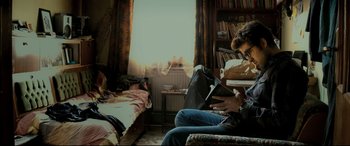 Movie still from “The Wild Pear Tree” (2018), directed by Nuri Bilge Ceylan – A man sitting on a chair reading a book in front of a bed; Medium shot, High angle