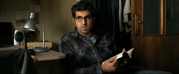 Movie still from “The Wild Pear Tree” (2018), directed by Nuri Bilge Ceylan – A man sitting on a couch holding a cell phone; Close Up shot, Over the shoulder angle