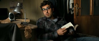 Movie still from “The Wild Pear Tree” (2018), directed by Nuri Bilge Ceylan – A man sitting in a room holding a book; Medium shot, Over the shoulder angle
