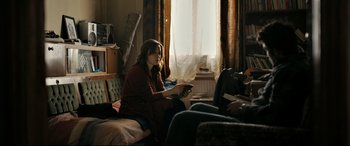 Movie still from “The Wild Pear Tree” (2018), directed by Nuri Bilge Ceylan – A woman sitting on a couch in a living room holding a tv remote control; Medium shot, Over the shoulder angle