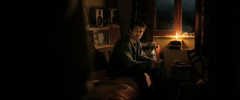 Movie still from “The Wild Pear Tree” (2018), directed by Nuri Bilge Ceylan – A man sitting on top of a bed next to a window; Medium shot, Over the shoulder angle