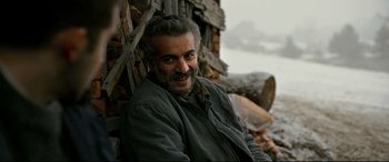 Movie still from “The Wild Pear Tree” (2018), directed by Nuri Bilge Ceylan – A man with a beard sitting in front of a wooden structure; Close Up shot, Low angle