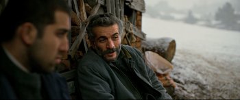 Movie still from “The Wild Pear Tree” (2018), directed by Nuri Bilge Ceylan – A man sitting in front of a pile of wood; Close Up shot, Over the shoulder angle