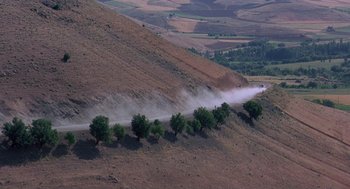 Movie still from “The Wind Will Carry Us” (1999), directed by Abbas Kiarostami – A group of trees that are on the side of a hill; Extreme Wide shot, High angle