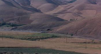 Movie still from “The Wind Will Carry Us” (1999), directed by Abbas Kiarostami – A car driving down a dirt road in the middle of a field; Extreme Wide shot, High angle