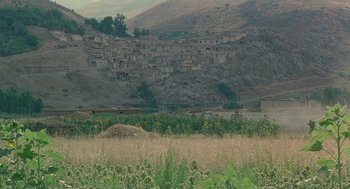 Movie still from “The Wind Will Carry Us” (1999), directed by Abbas Kiarostami – A view of a mountain with a bunch of houses in the background; Extreme Wide shot, High angle