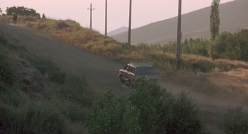 Movie still from “The Wind Will Carry Us” (1999), directed by Abbas Kiarostami – An suv driving down a dirt road in the middle of nowhere; Extreme Wide shot, High angle