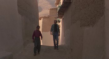 Movie still from “The Wind Will Carry Us” (1999), directed by Abbas Kiarostami – Two men are walking down a narrow alley way; Wide shot, High angle