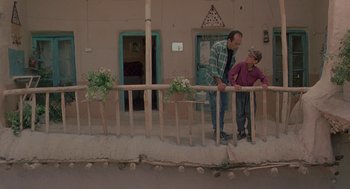 Movie still from “The Wind Will Carry Us” (1999), directed by Abbas Kiarostami – Two men standing on the side of the street; Wide shot, High angle