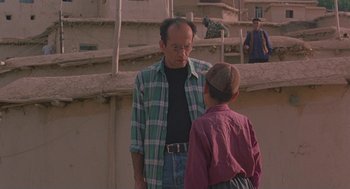 Movie still from “The Wind Will Carry Us” (1999), directed by Abbas Kiarostami – A man and a boy are standing together; Medium shot, Over the shoulder angle