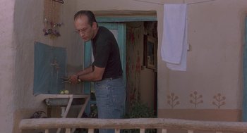 Movie still from “The Wind Will Carry Us” (1999), directed by Abbas Kiarostami – A man in black shirt and blue jeans cooking food; Medium shot, Low angle