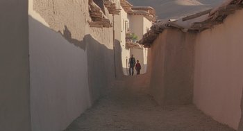 Movie still from “The Wind Will Carry Us” (1999), directed by Abbas Kiarostami – Two people walking down a narrow alley way; Extreme Wide shot, Low angle
