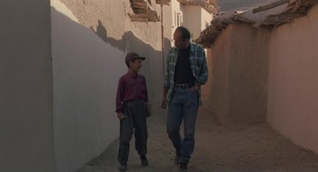 Movie still from “The Wind Will Carry Us” (1999), directed by Abbas Kiarostami – A man and a boy walking down a street; Wide shot, Low angle