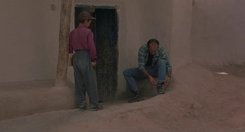 Movie still from “The Wind Will Carry Us” (1999), directed by Abbas Kiarostami – Two men are standing in front of a doorway; Wide shot, Low angle