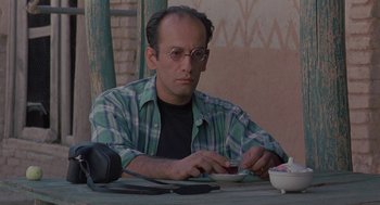 Movie still from “The Wind Will Carry Us” (1999), directed by Abbas Kiarostami – A man sitting at a table looking at a cell phone; Close Up shot, Low angle
