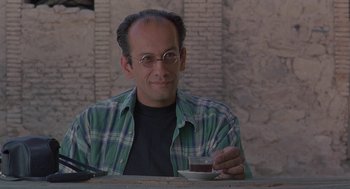 Movie still from “The Wind Will Carry Us” (1999), directed by Abbas Kiarostami – A man sitting at a table holding a cup of coffee; Close Up shot, Low angle