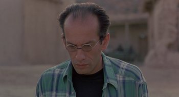 Movie still from “The Wind Will Carry Us” (1999), directed by Abbas Kiarostami – A person wearing glasses and a plaid shirt; Close Up shot, Low angle