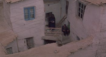 Movie still from “The Wind Will Carry Us” (1999), directed by Abbas Kiarostami – Two men sitting on steps in an old building; Wide shot, High angle