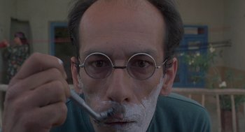 Movie still from “The Wind Will Carry Us” (1999), directed by Abbas Kiarostami – A man with glasses is shaving his face with a toothbrush; Extreme Close Up shot, Low angle